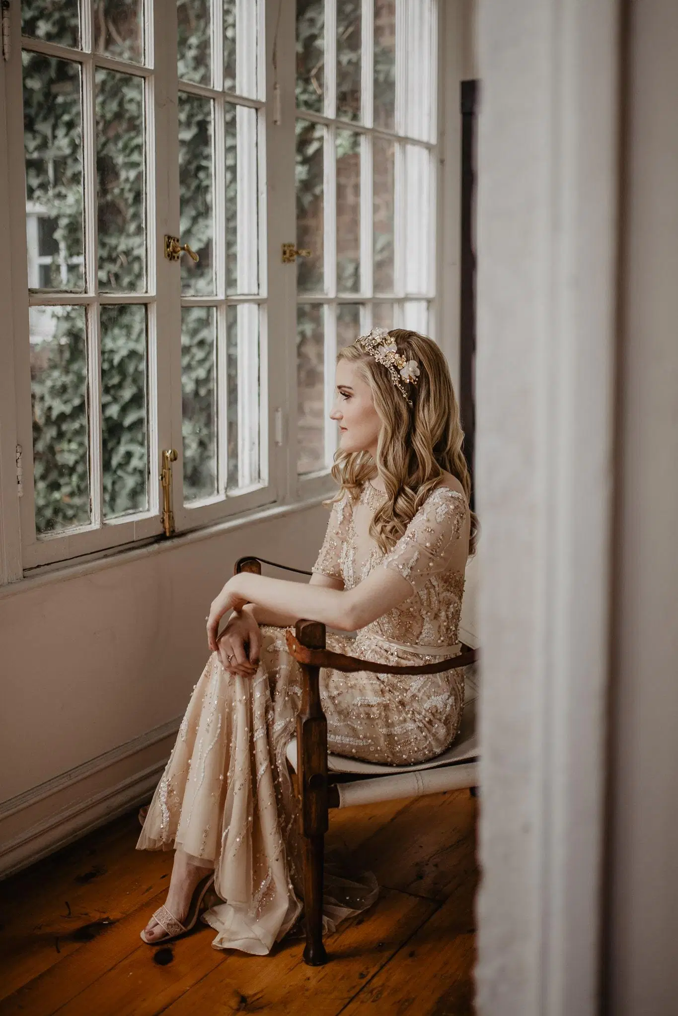Bride sitting in chair in front of window in her wedding gown on her wedding day