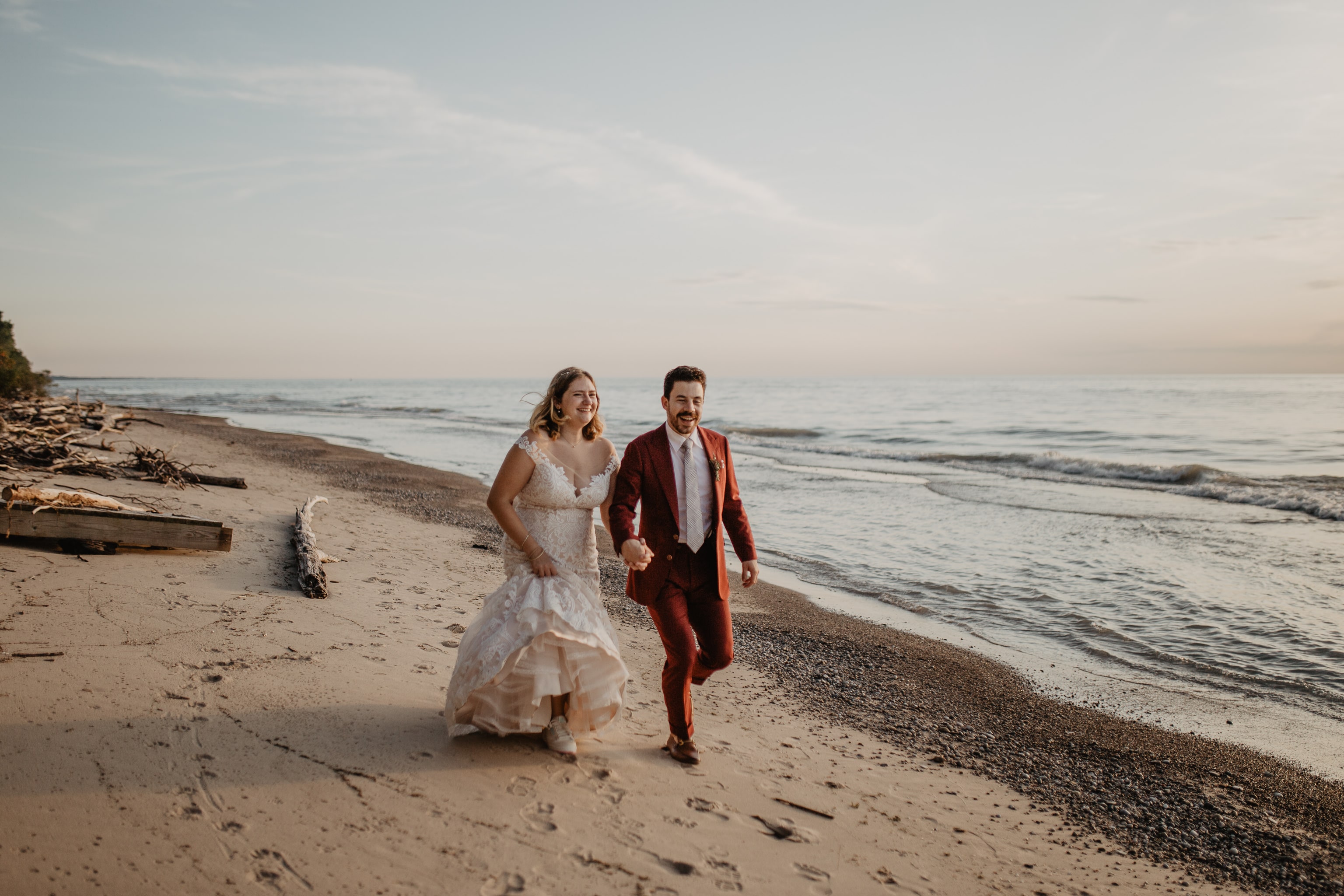 Bride and groom running on beach at sunset