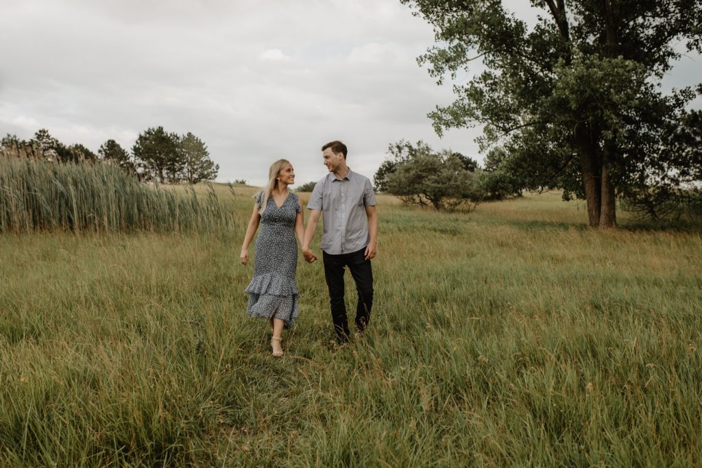 Couple walking through tall grassy field holding hands