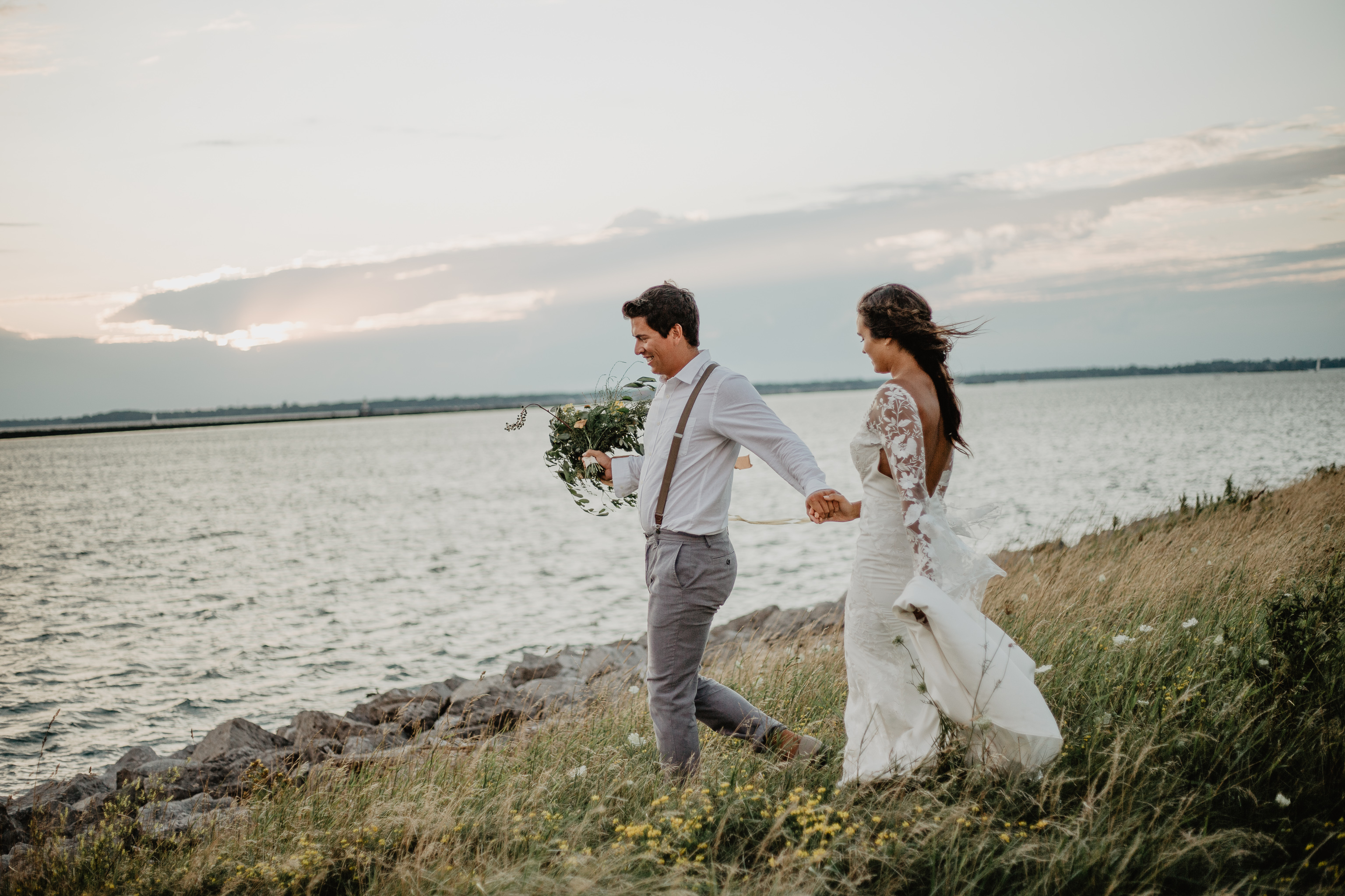 Bride and Groom walking through wildflowers with waterfront behind them in Buffalo, NY