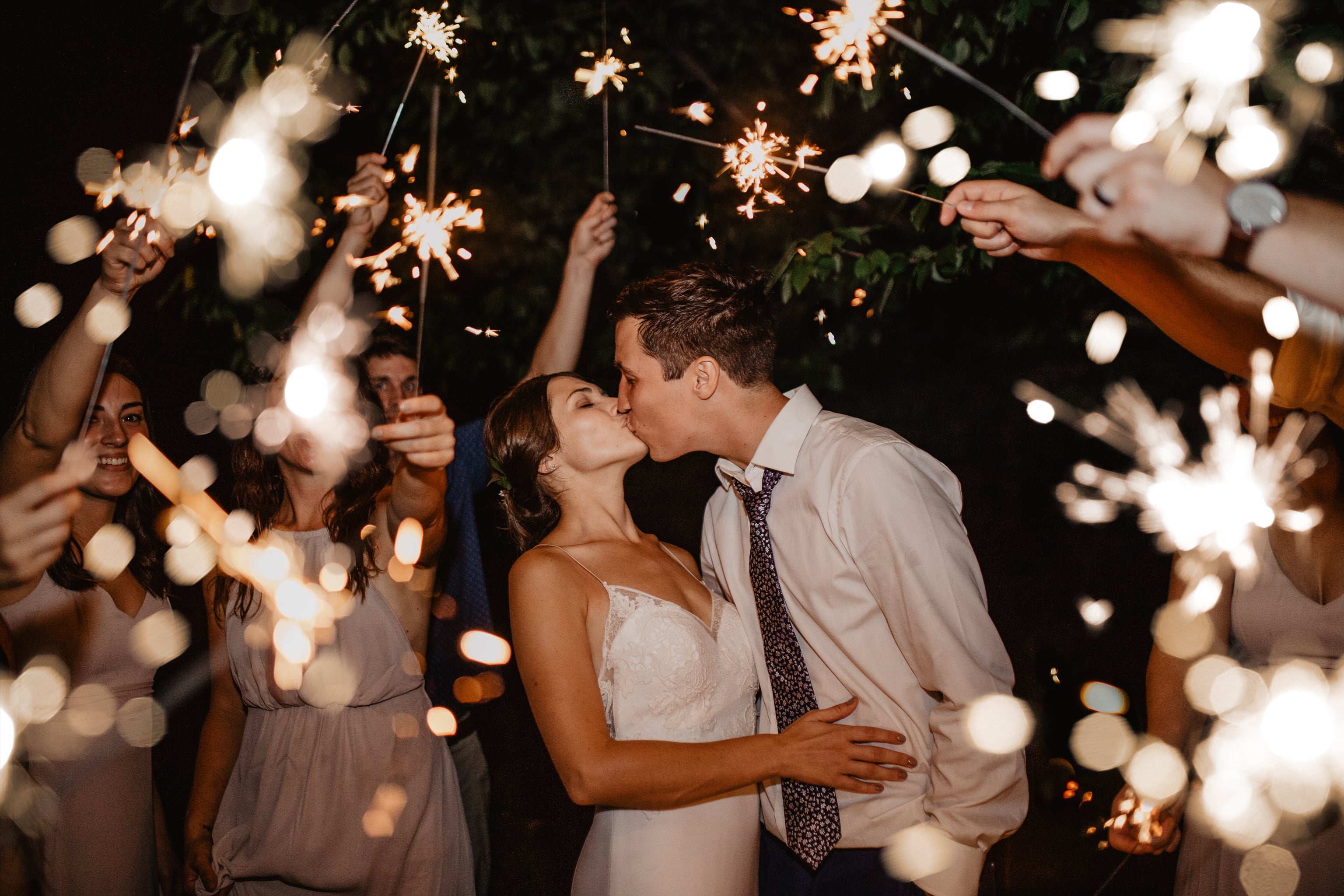 Bride and Groom kiss on their wedding night surrounded by guests with bright sparklers as they exit