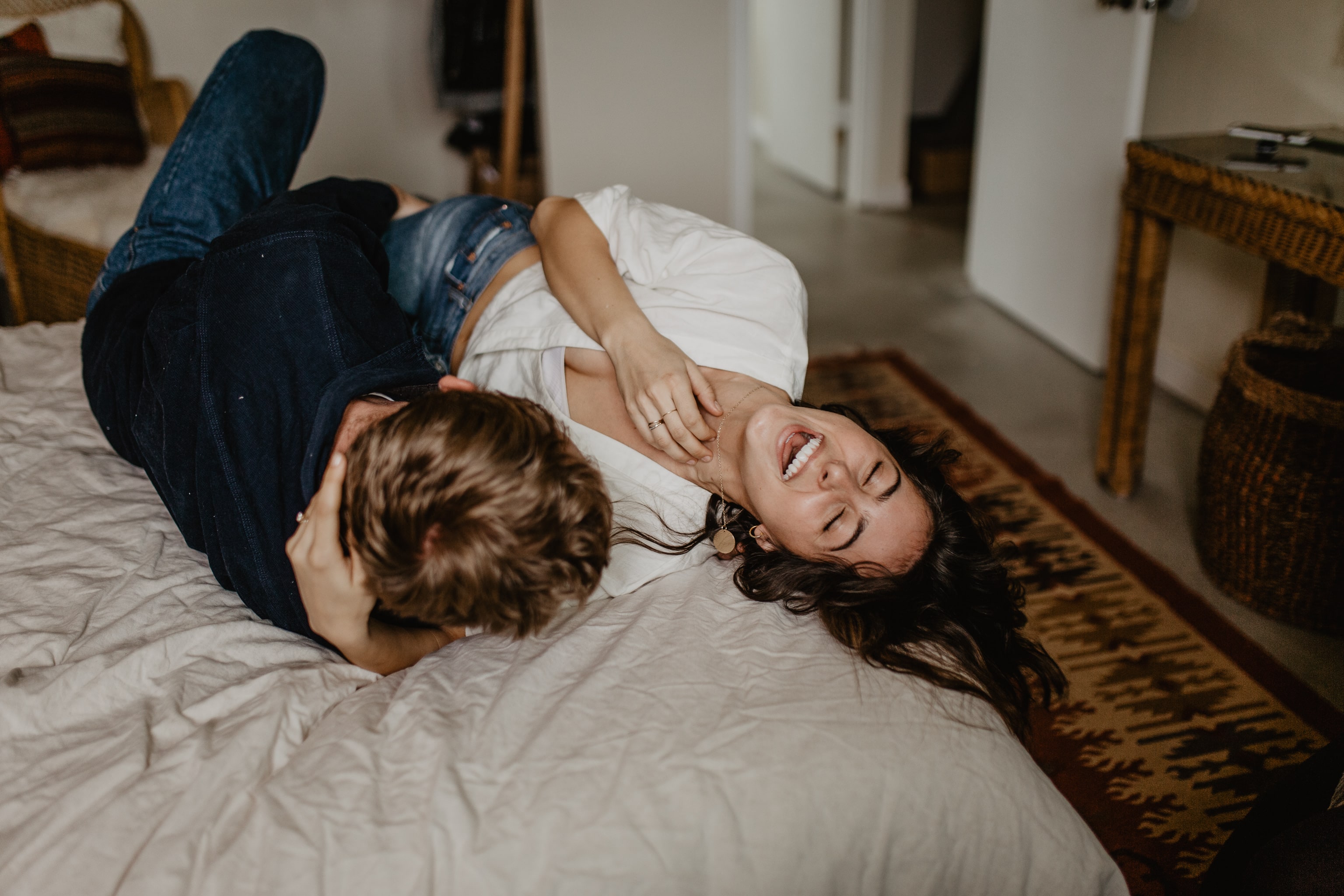 Girl laughing on bed as fiancé hugs her during an in home engagement session with Buffalo based photographer Jessy Herman Photo