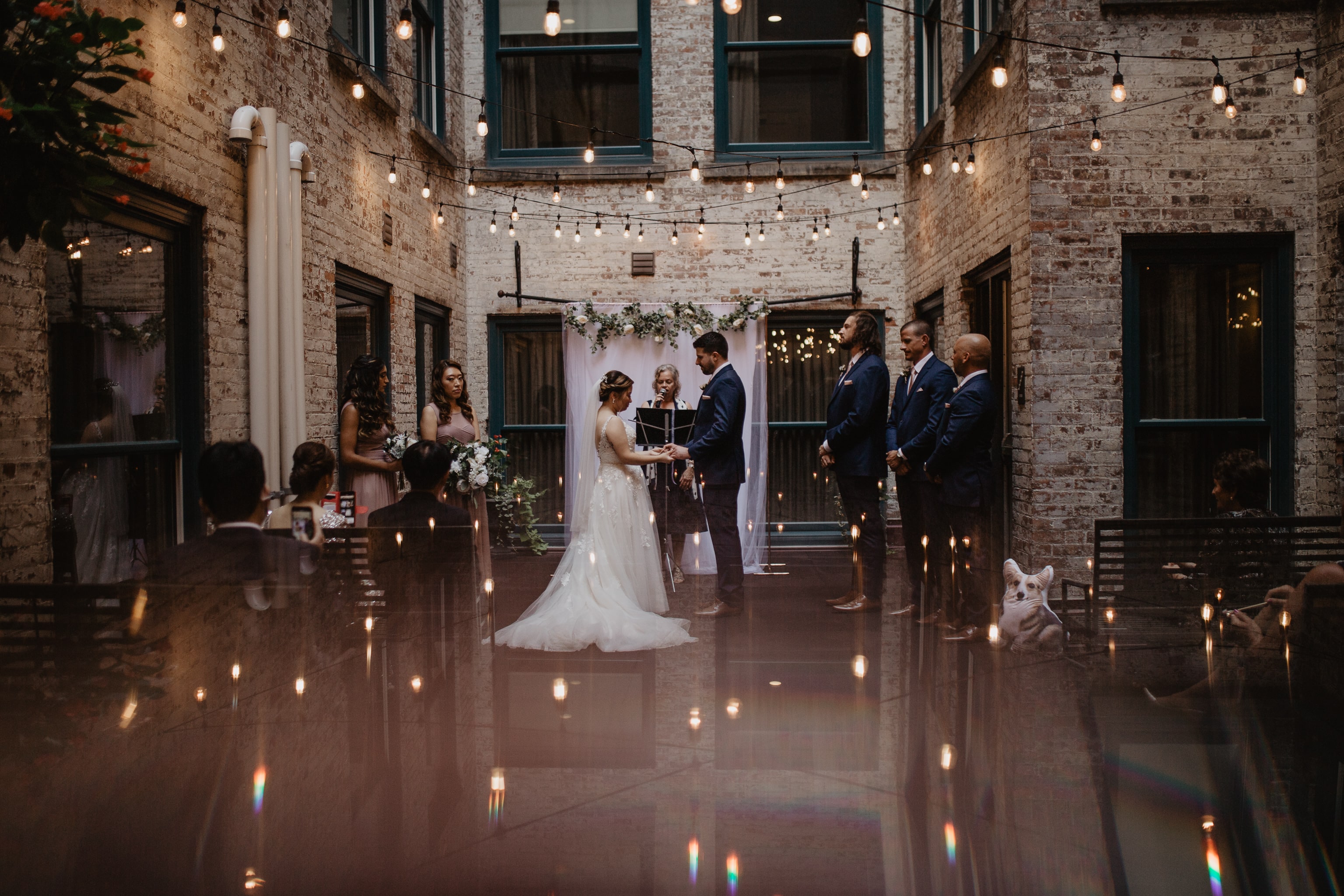 Couple during wedding ceremony in brick courtyard surrounded by twinkling string lights