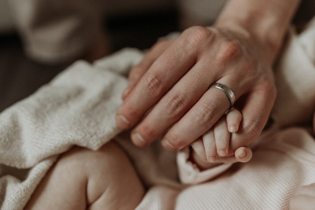 Close up photo of newborn baby wrapping fingers around her dads hand during family photos taken by Buffalo photographer Jessy Herman Photo