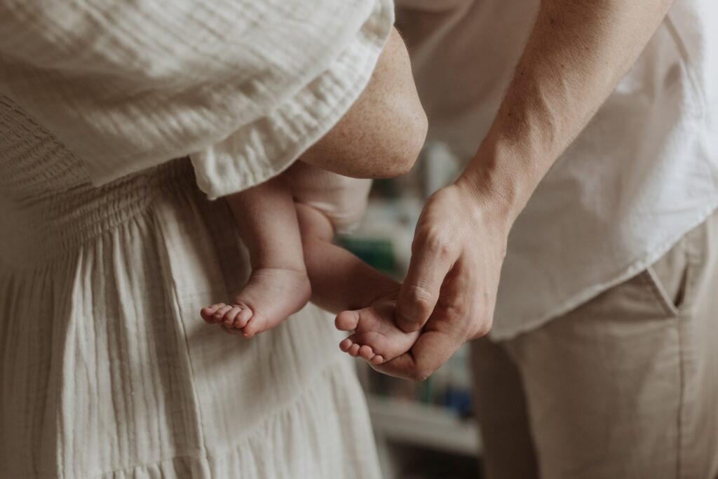 A detail photo of a mom holding her newborn baby while dad holds her feet during family photos taken by Buffalo photographer Jessy Herman Photo