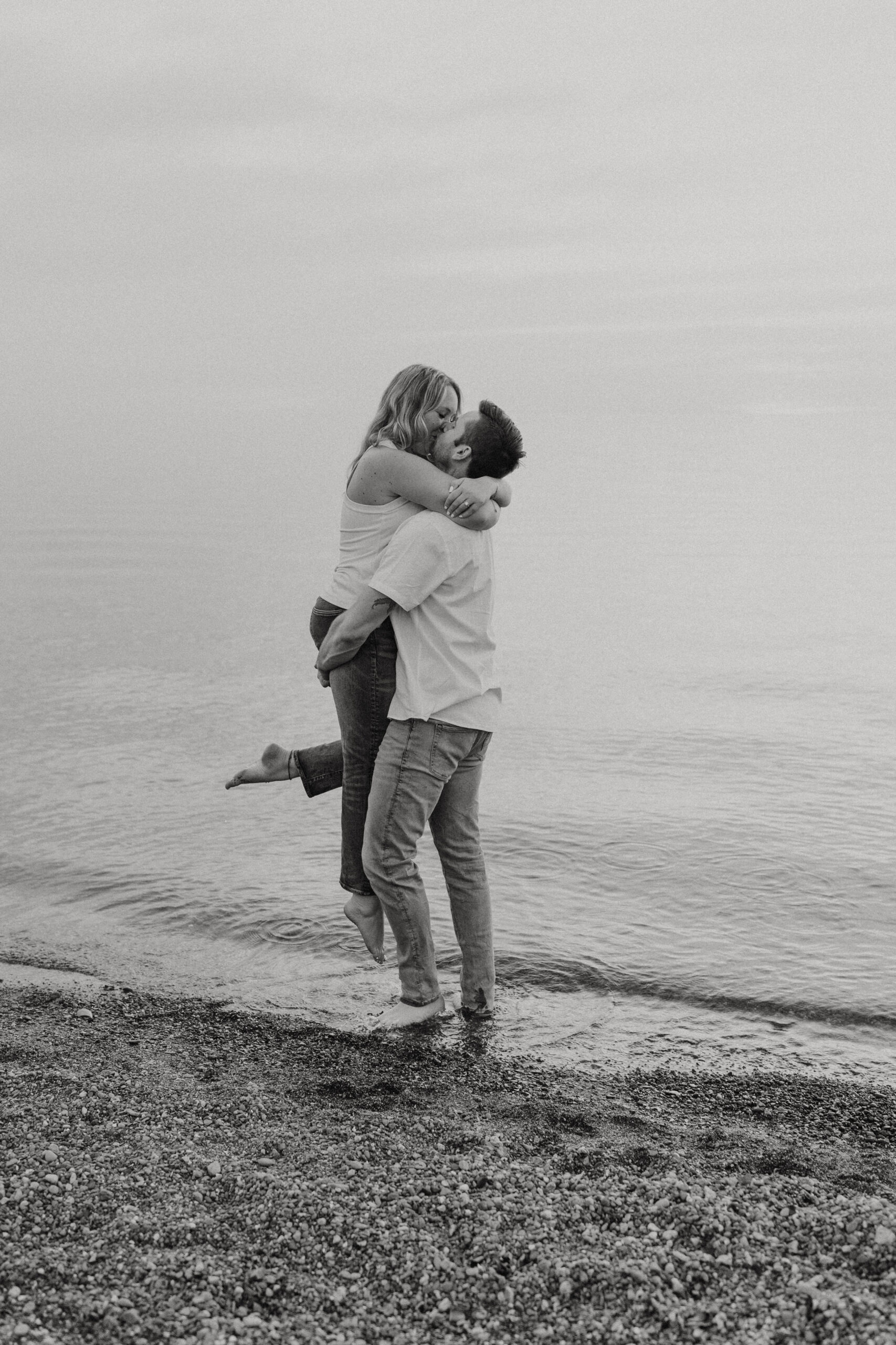 Black and white photo of couple kissing at beach during engagement photos by Jessy Herman Photo