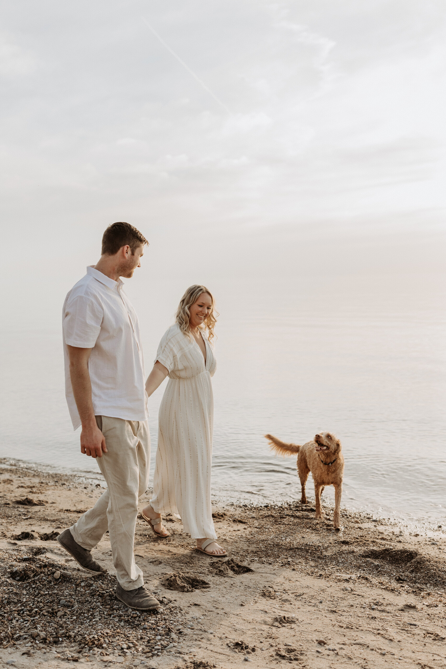 Couple walks on beach during engagement session on Lake Erie in Buffalo, NY with dog