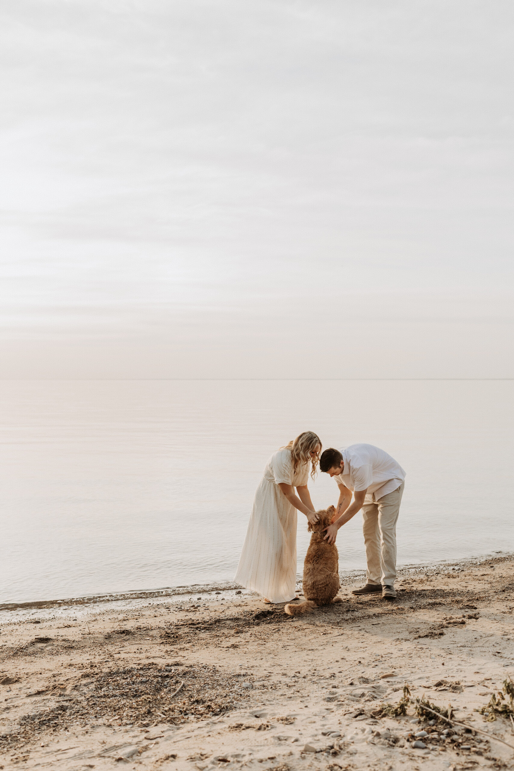 Couple pets their dog at the beach during engagement photos at Lake Erie in Buffalo, NY with Jessy Herman Photo