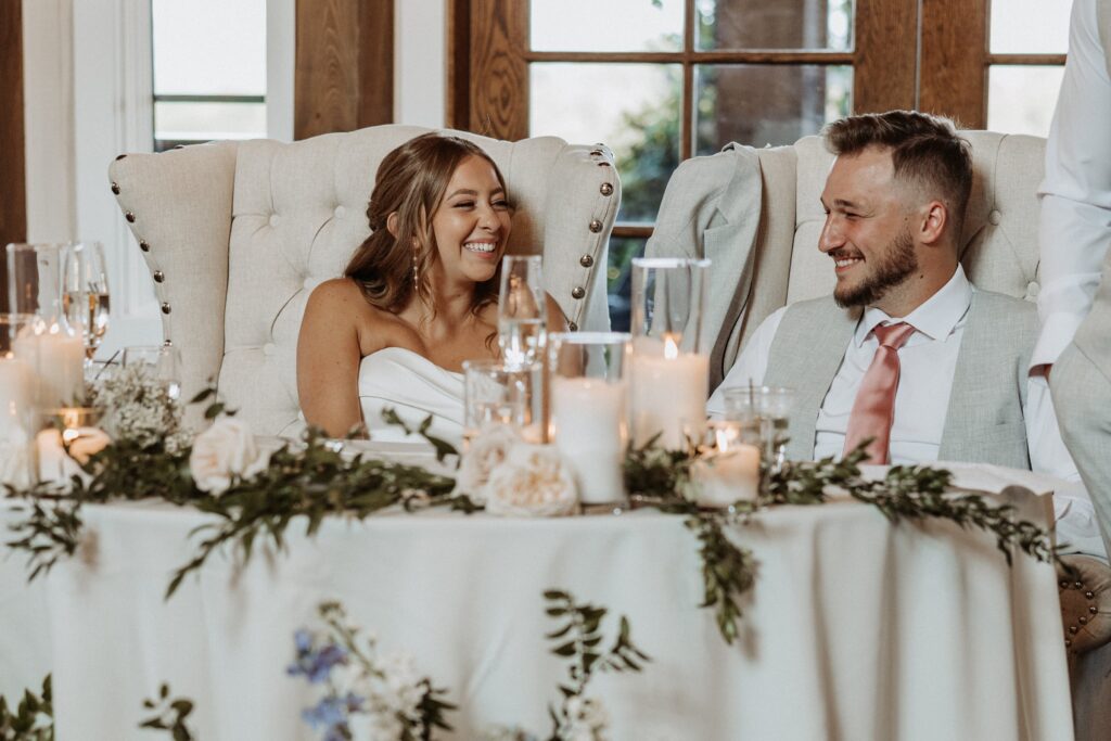 Bride and groom smiling during speeches at their wedding